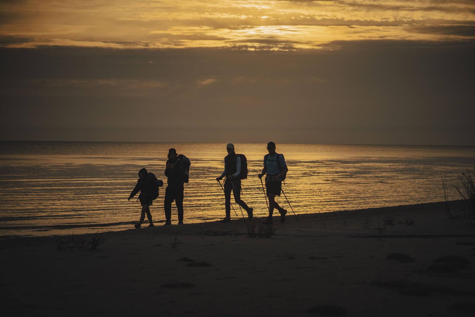 Silhouettes of four people walking by the sea in sunset