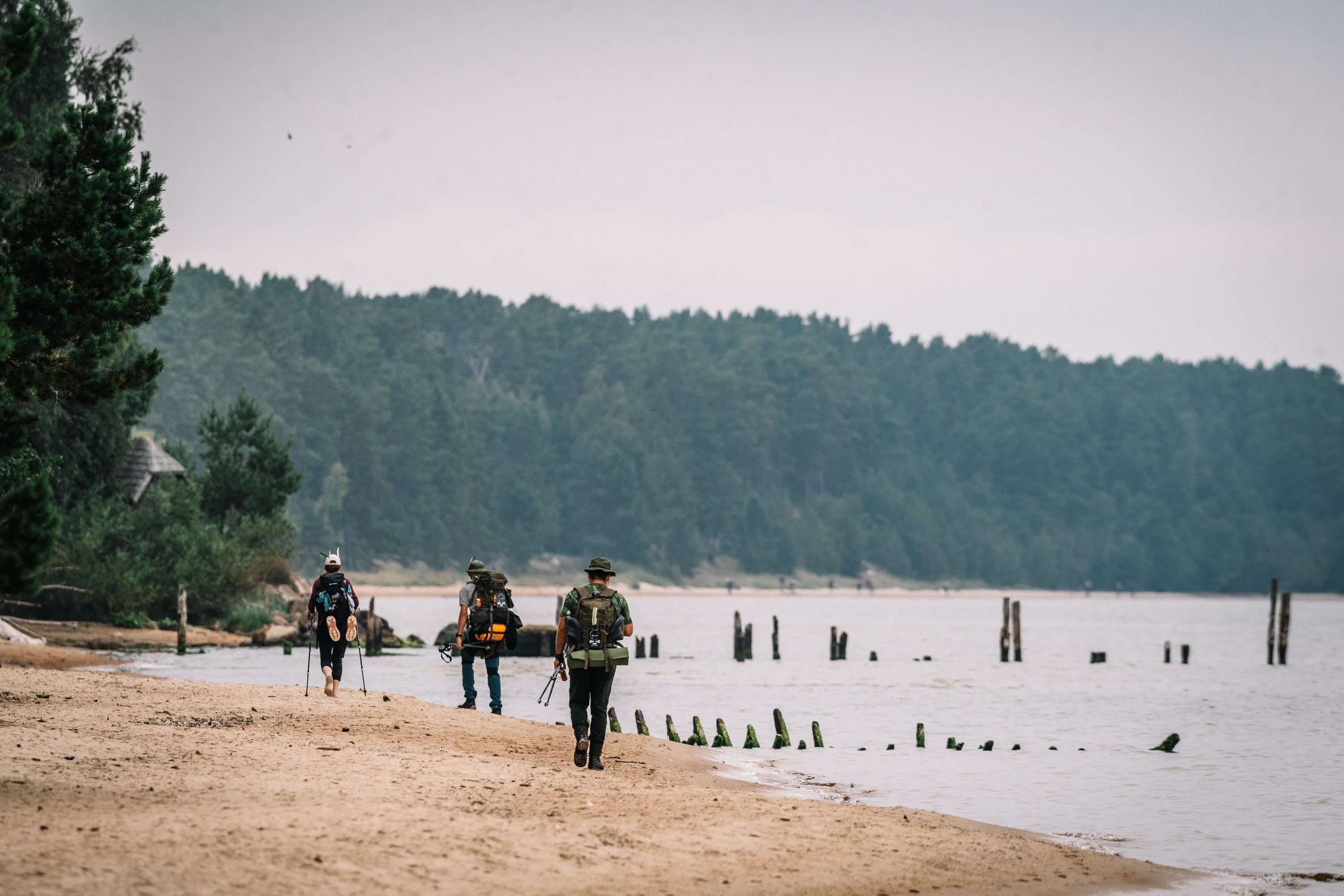 Pārgājiena dalībniece atgūlusies uz soliņa autobusa pieturā, fonā priežu mežs